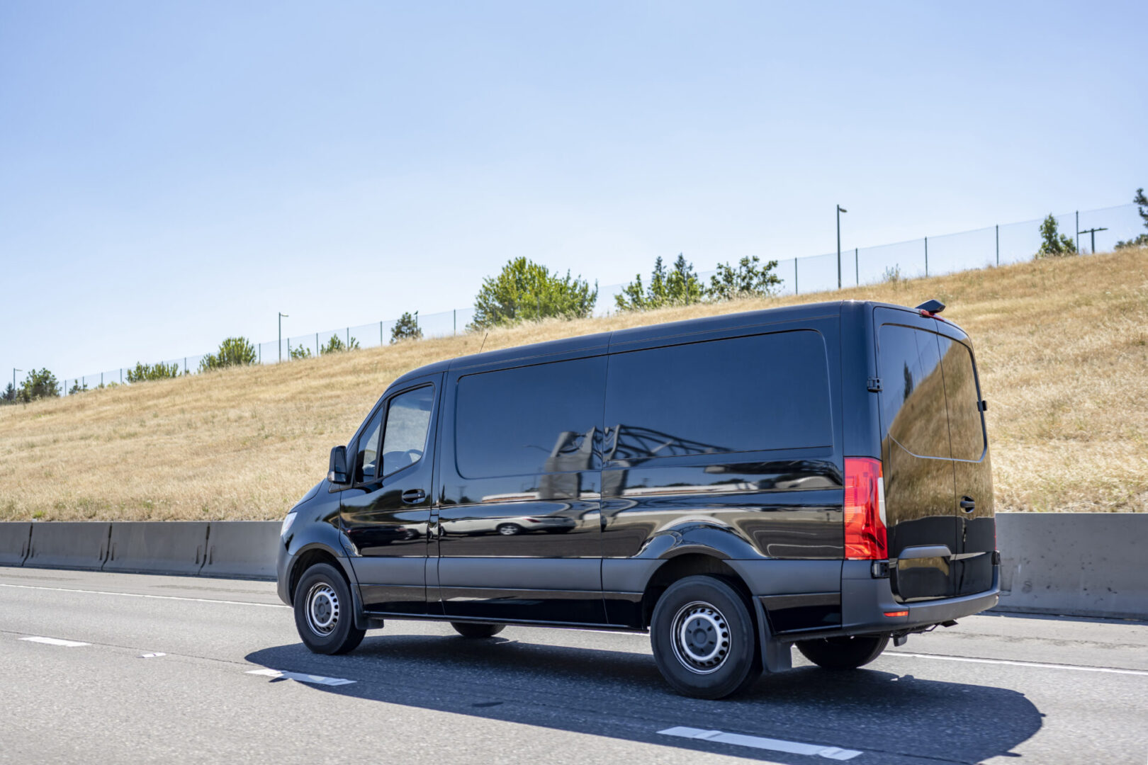 Compact industrial small size black mini van with cargo compartment for local deliveries and small business needs running on the wide multiline highway road for customers commercial cargo delivery