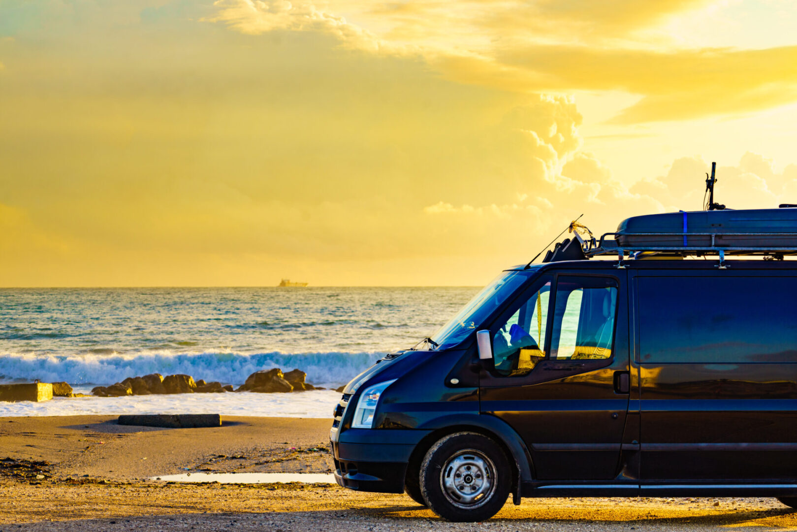 A camper van parked by the beach at sunset with golden skies.