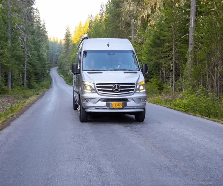 A silver van driving on a forest road during daylight.
